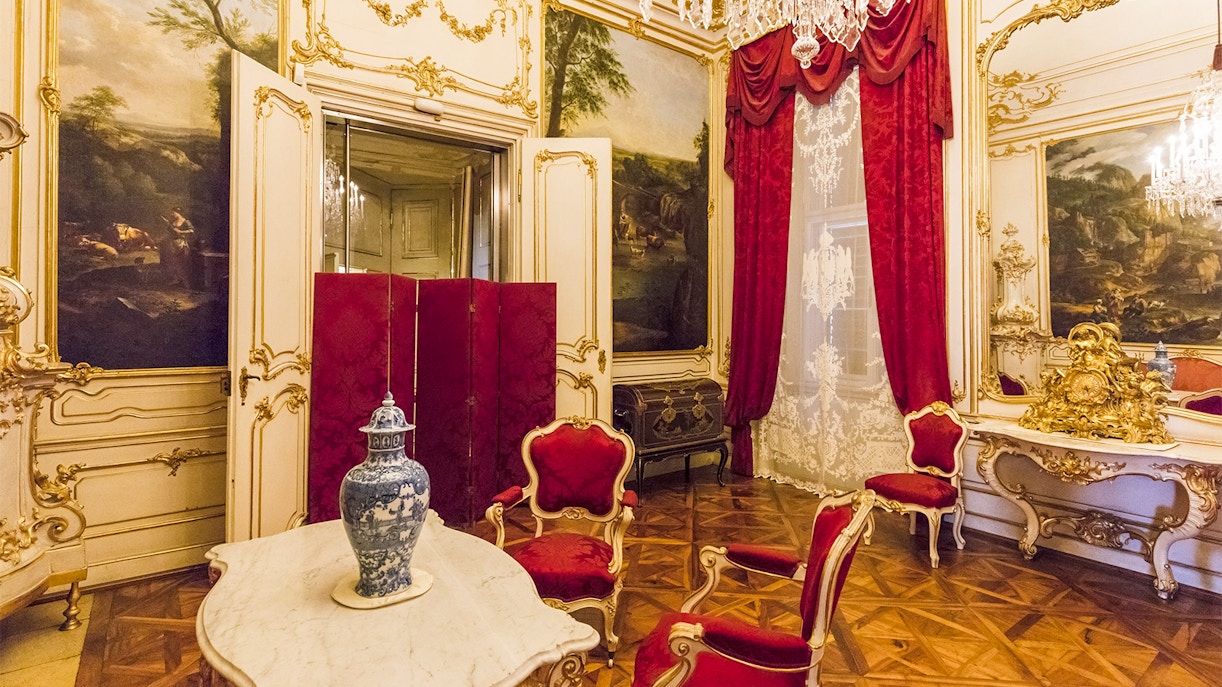 Elegant room in Schönbrunn Palace, Vienna, featuring ornate decor and red velvet chairs.