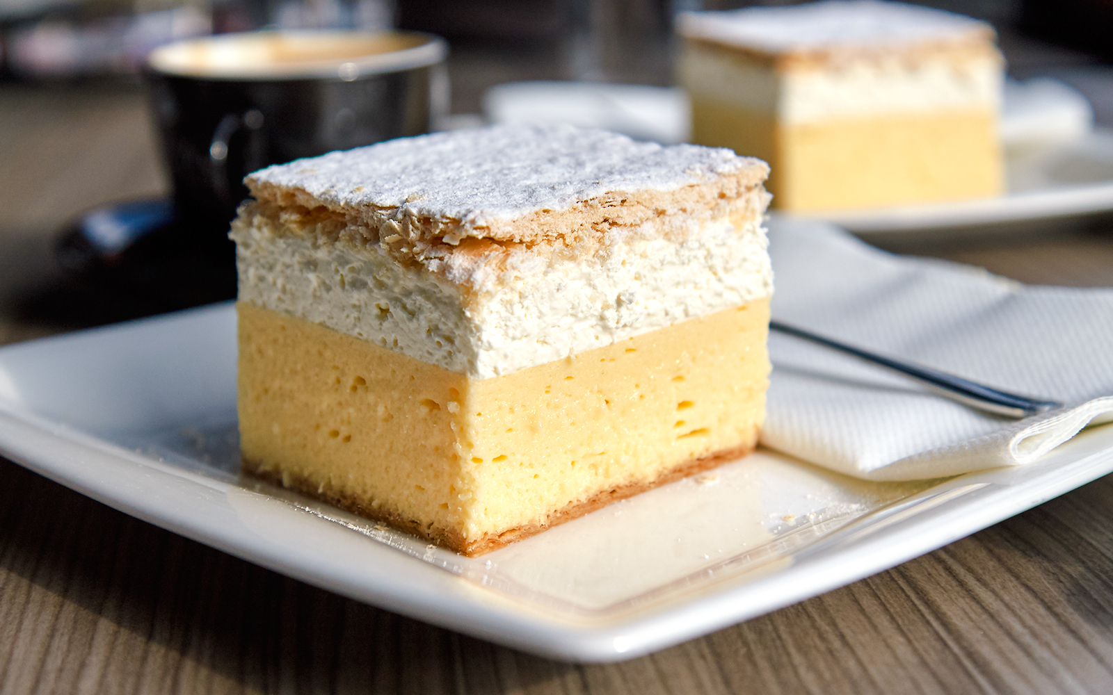 Bled cream cake on a plate with a cup of coffee in the background.