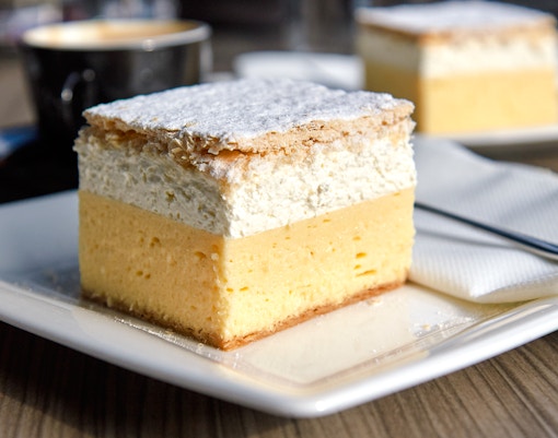 Bled cream cake on a plate with a cup of coffee in the background.