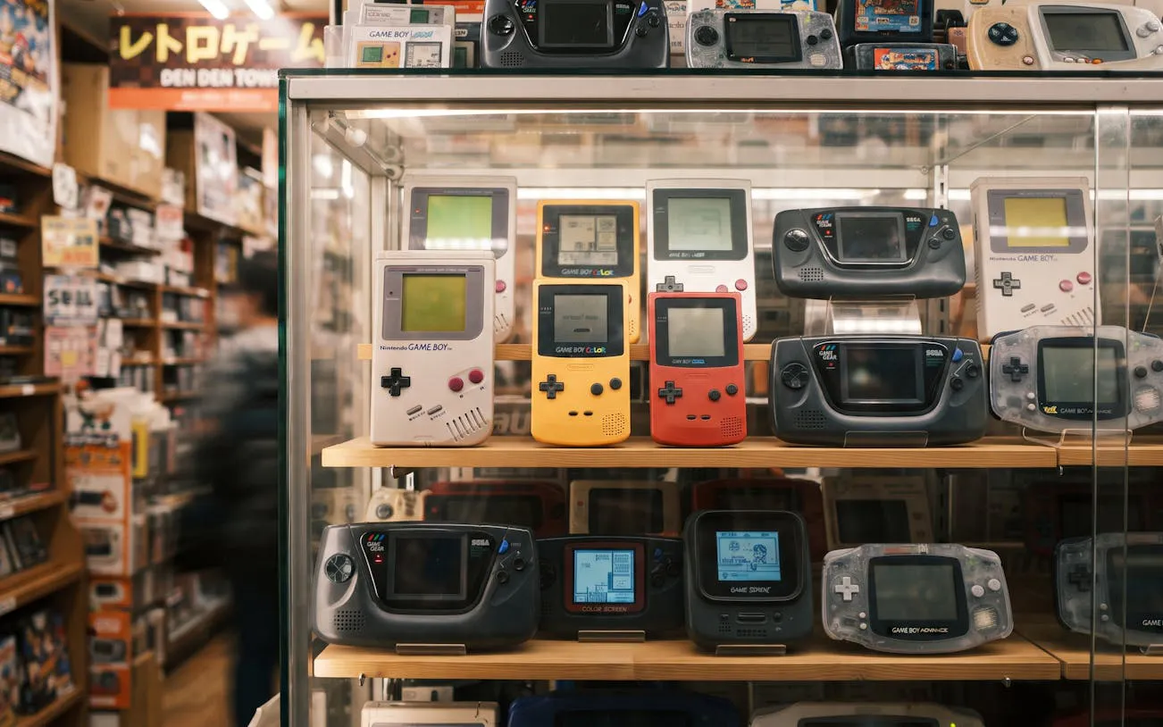 Retro gaming consoles displayed in a glass case at Osaka Den Den Town shop.
