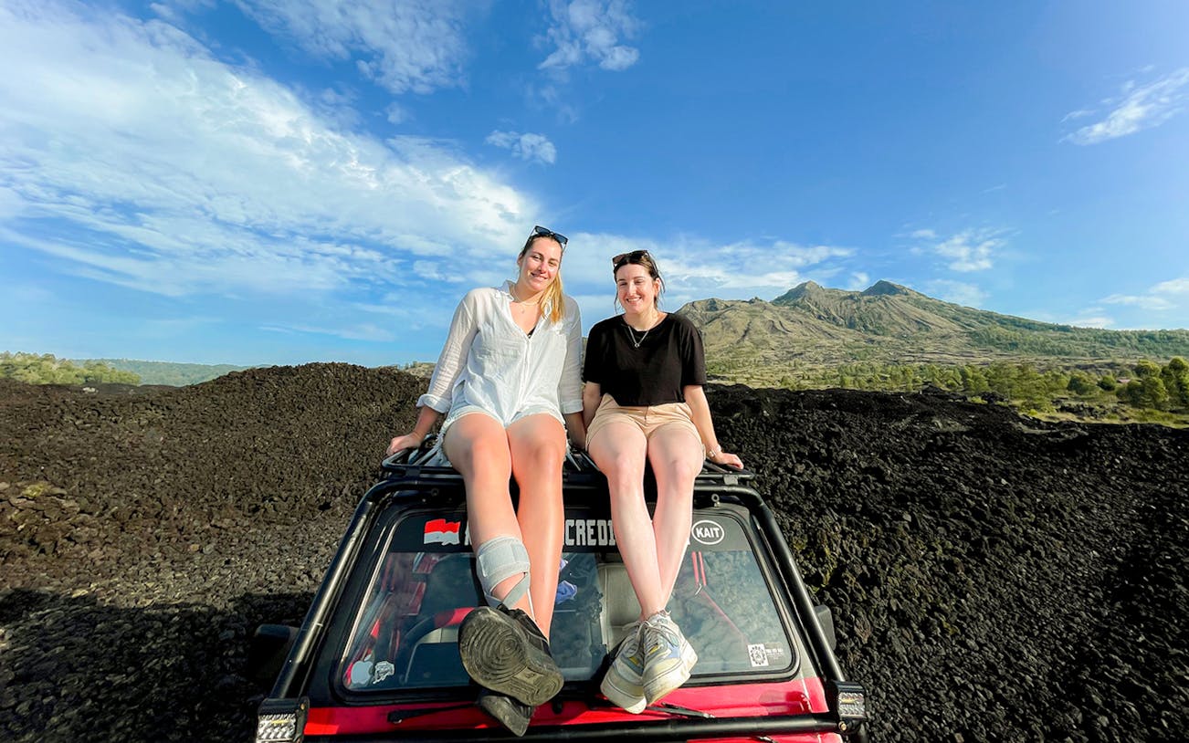 Two people sitting on a jeep with Mount Batur in the background during a sunrise tour.