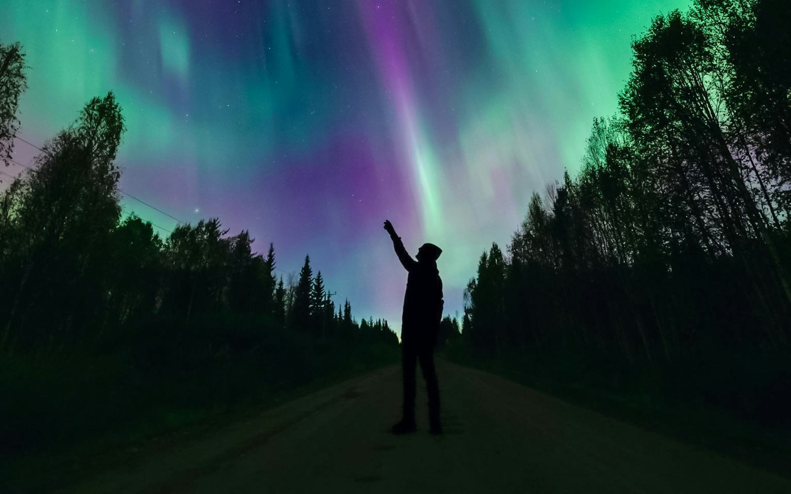 Silhouette of person pointing at Northern Lights in Levi, Finland.