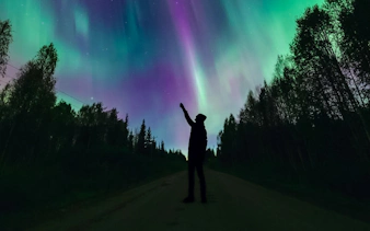 Silhouette of person pointing at Northern Lights in Levi, Finland.