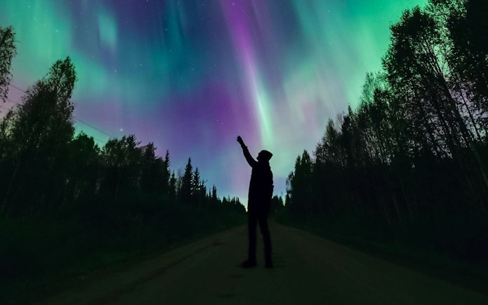 Silhouette of person pointing at Northern Lights in Levi, Finland.
