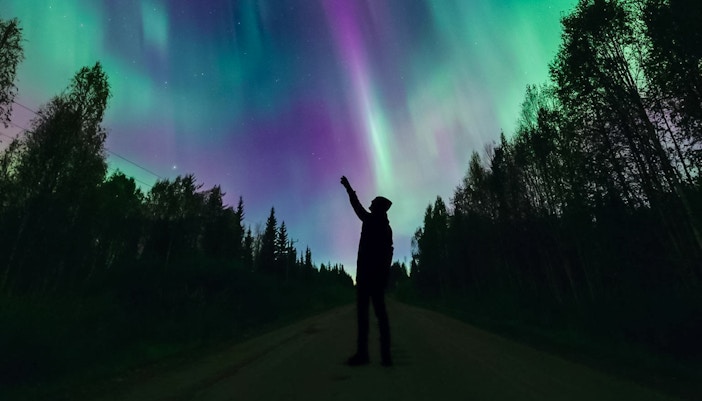 Silhouette of person pointing at Northern Lights in Levi, Finland.