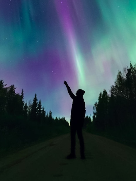 Silhouette of person pointing at Northern Lights in Levi, Finland.
