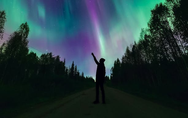 Silhouette of person pointing at Northern Lights in Levi, Finland.