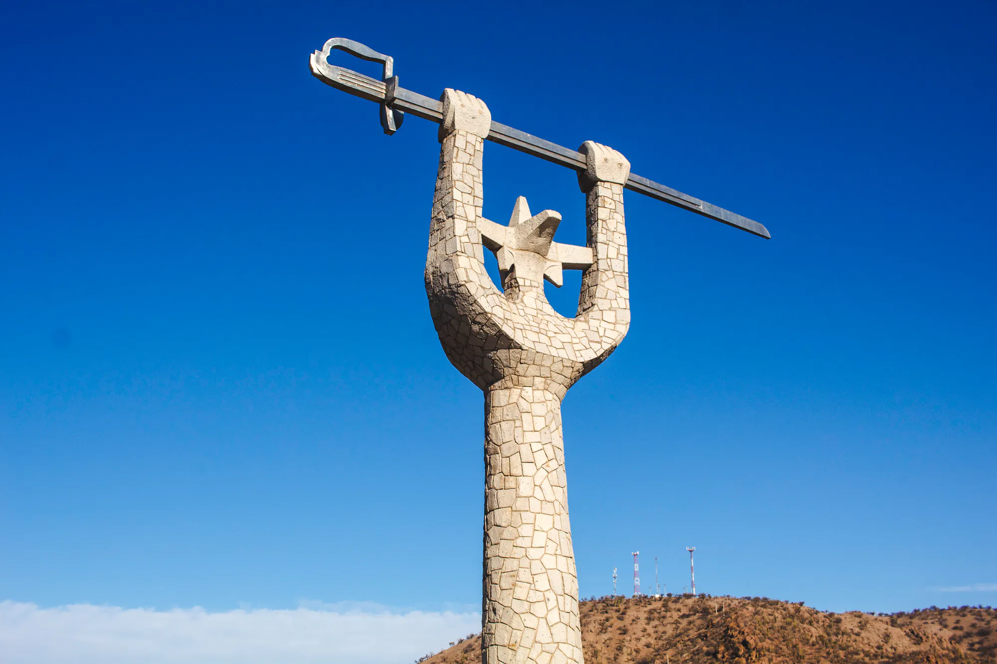 Stone monument with arms raised holding a sword against a clear blue sky near Portillo, Chile.