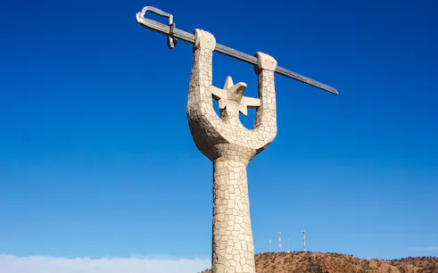 Stone monument with arms raised holding a sword against a clear blue sky near Portillo, Chile.
