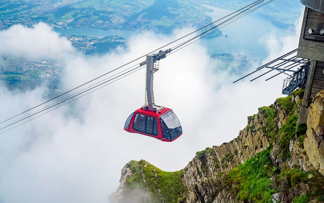 Cable car ascending through clouds at Fräkmüntegg, offering views of Swiss landscape.