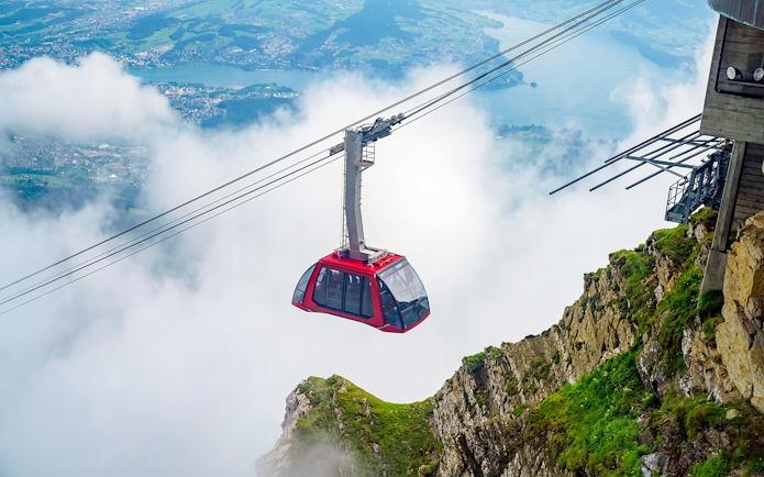 Cable car ascending through clouds at Fräkmüntegg, offering views of Swiss landscape.