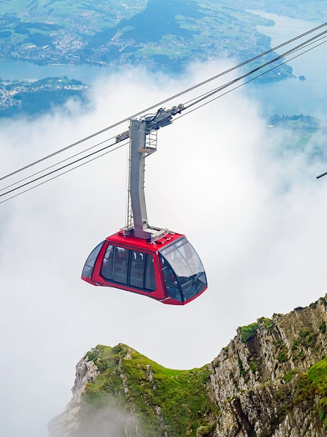 Cable car ascending through clouds at Fräkmüntegg, offering views of Swiss landscape.