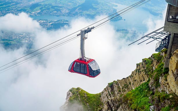 Cable car ascending through clouds at Fräkmüntegg, offering views of Swiss landscape.