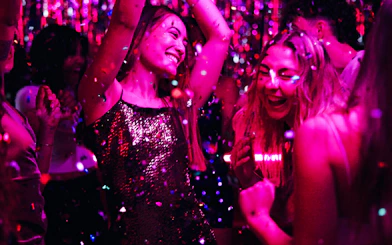 People dancing and celebrating at a vibrant nightclub with colorful lights.