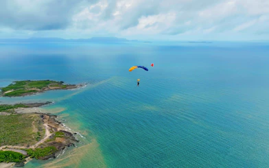 Skydiver descending over ocean near Airlie Beach with parachute.