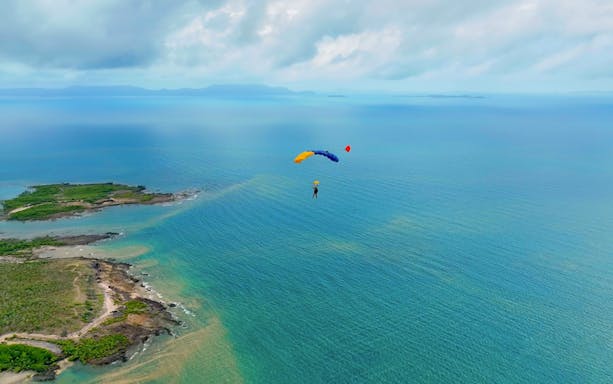 Skydiver descending over ocean near Airlie Beach with parachute.