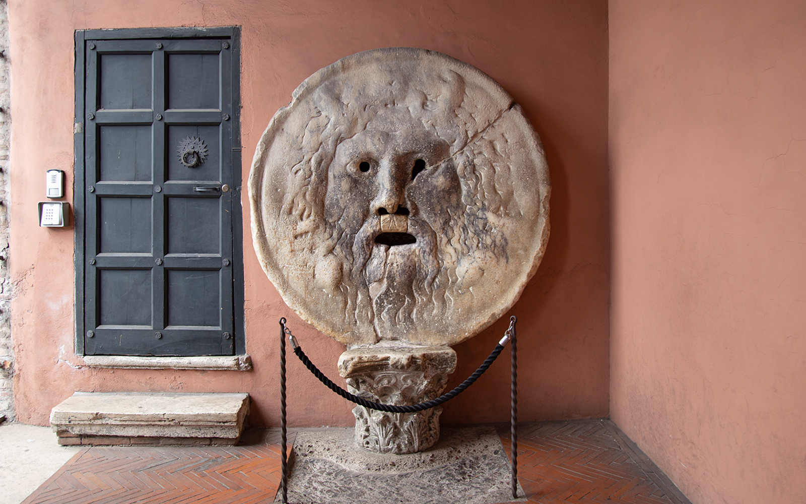 Mouth of Truth sculpture in Rome, Italy, next to a black door.