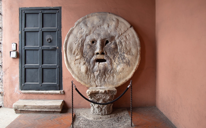 Mouth of Truth sculpture in Rome, Italy, next to a black door.