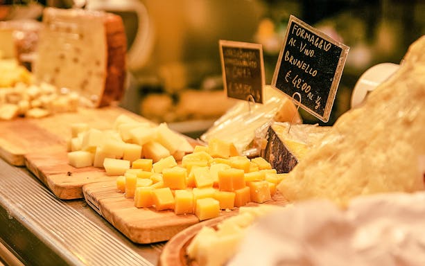 Cheese selection on wooden boards in a store with price tags.