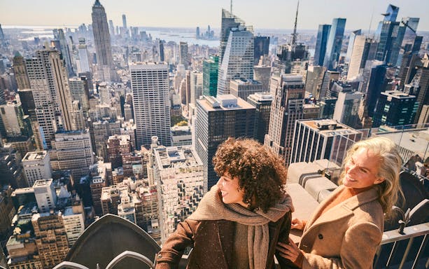 Visitors enjoying the view from Top of the Rock, New York City skyline in background.