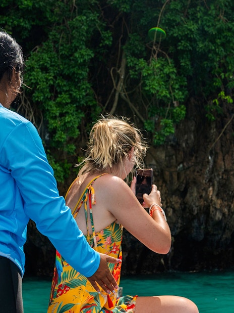 Tour guide assists guest taking photo of limestone karsts on Phi Phi Island speedboat tour.