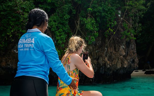 Tour guide assists guest taking photo of limestone karsts on Phi Phi Island speedboat tour.
