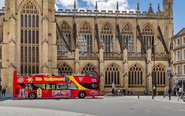 Red double-decker bus in front of Bath Abbey on the Bath Hop-On Hop-Off Tour.