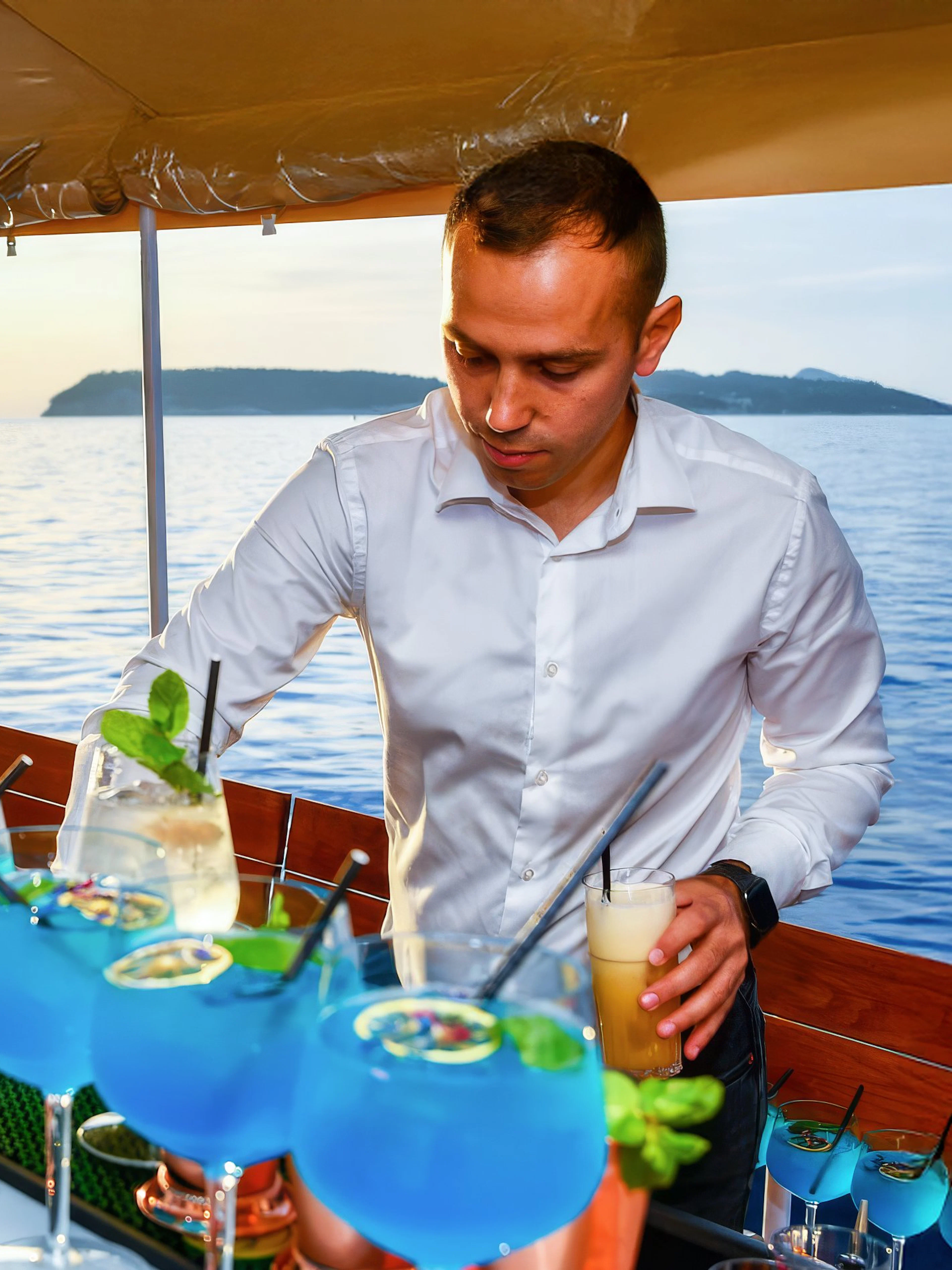 Mixologist serving blue cocktails on a boat with ocean view.