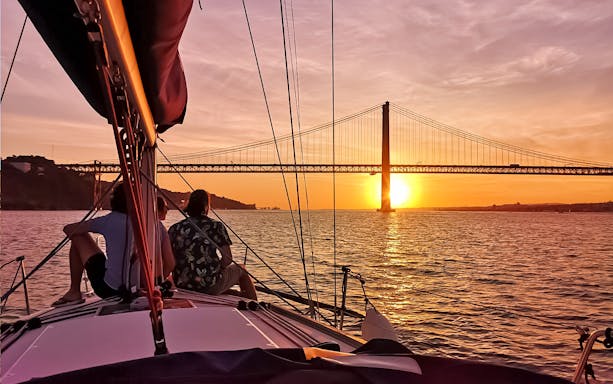 Sailing on the Tagus River at sunset with view of 25 de Abril Bridge in Lisbon.