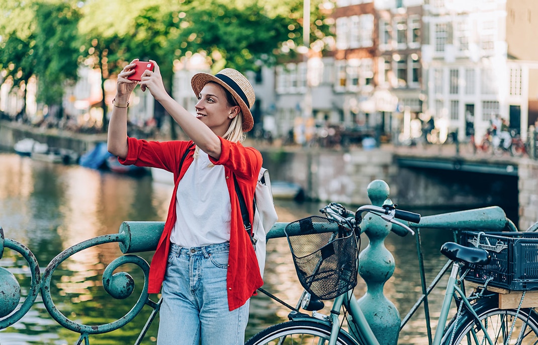 Woman taking a photo by a canal with a bicycle in Amsterdam.