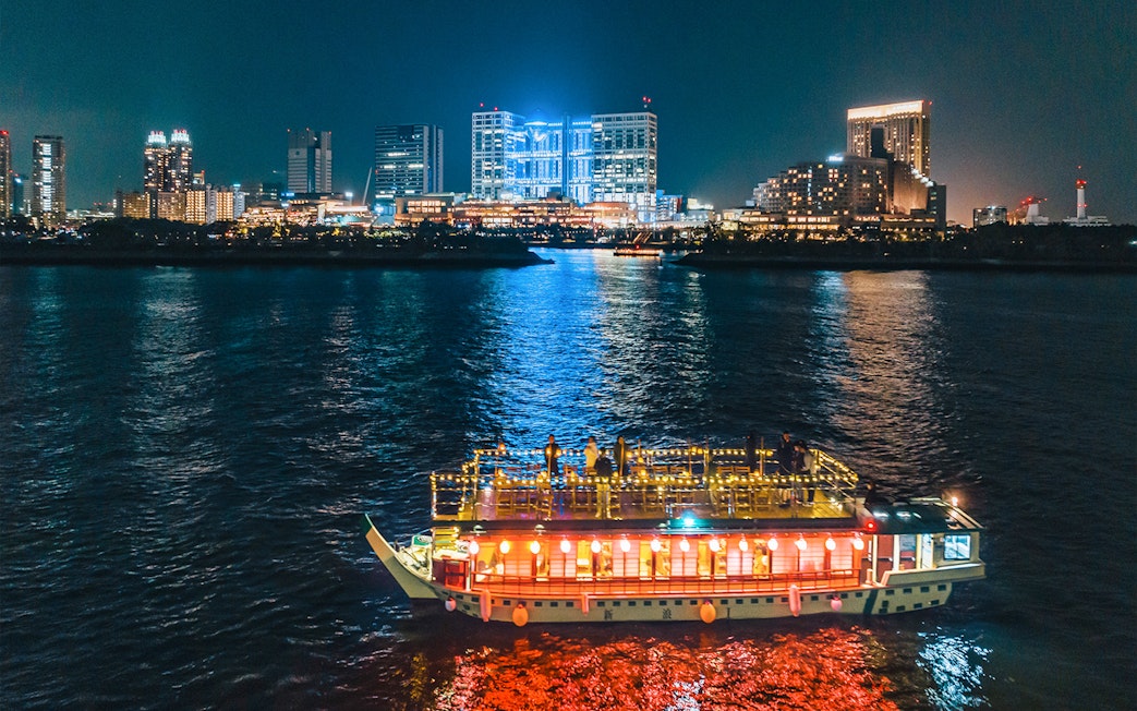 Yakatabune boat on Tokyo Bay at night with city skyline in background.