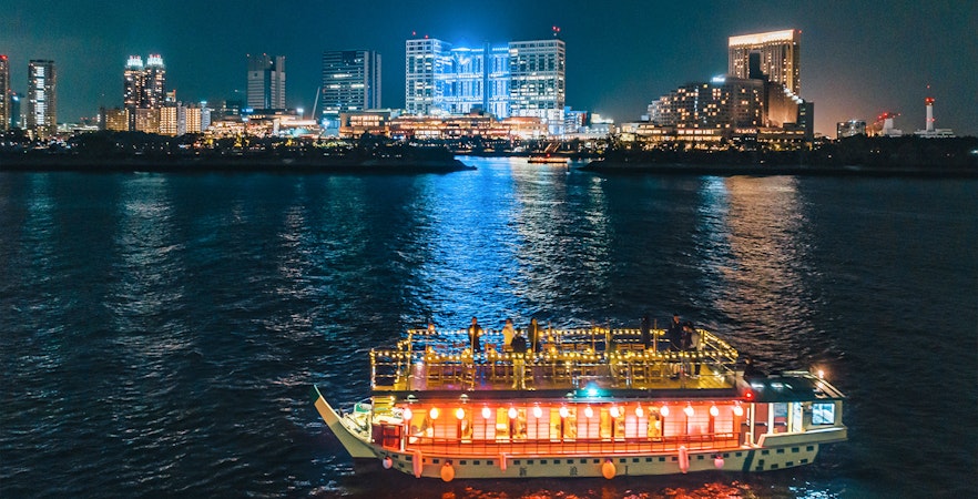 Yakatabune boat on Tokyo Bay at night with city skyline in background.