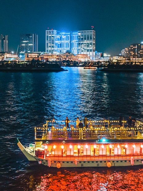 Yakatabune boat on Tokyo Bay at night with city skyline in background.