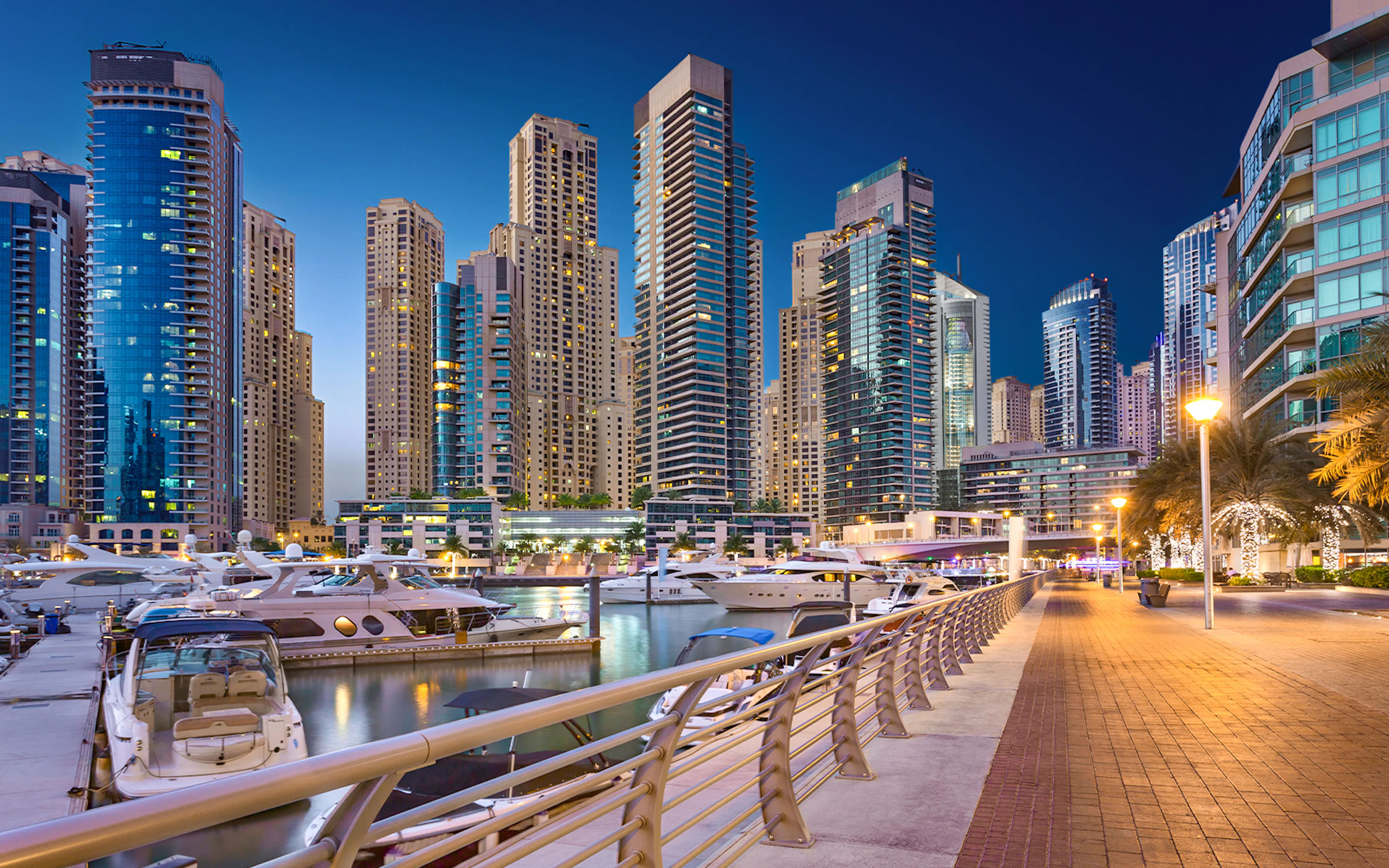 Dubai Marina Walk with yachts and skyscrapers at dusk.