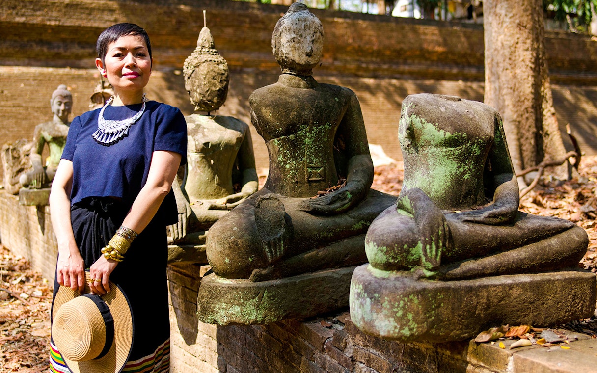 Female standing beside ancient Buddhist sculptures in a historical park.