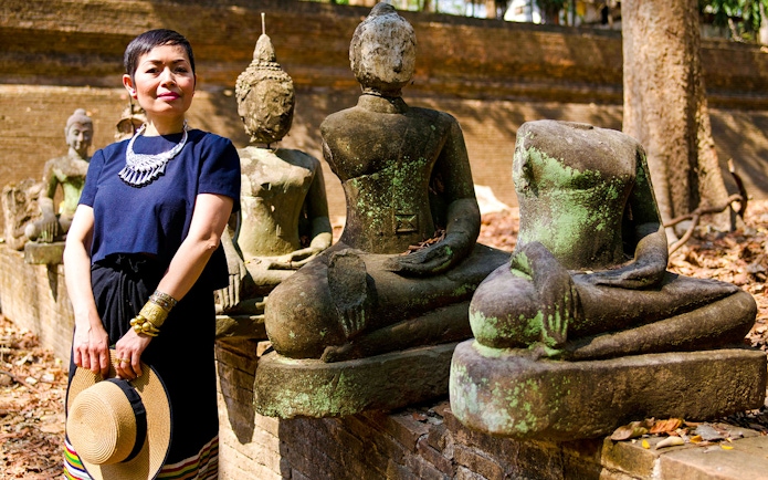 Female standing beside ancient Buddhist sculptures in a historical park.