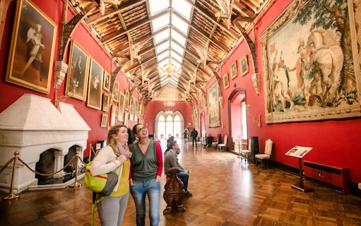 Visitors exploring the art-filled gallery of Kilkenny Castle with ornate ceiling and historic paintings.