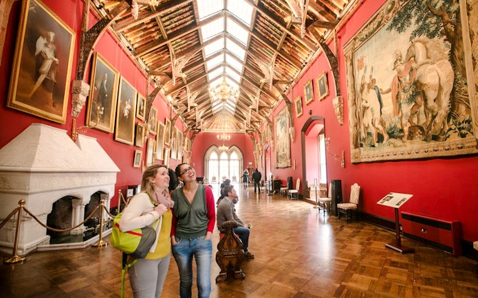 Visitors exploring the art-filled gallery of Kilkenny Castle with ornate ceiling and historic paintings.