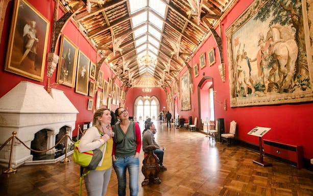 Visitors exploring the art-filled gallery of Kilkenny Castle with ornate ceiling and historic paintings.