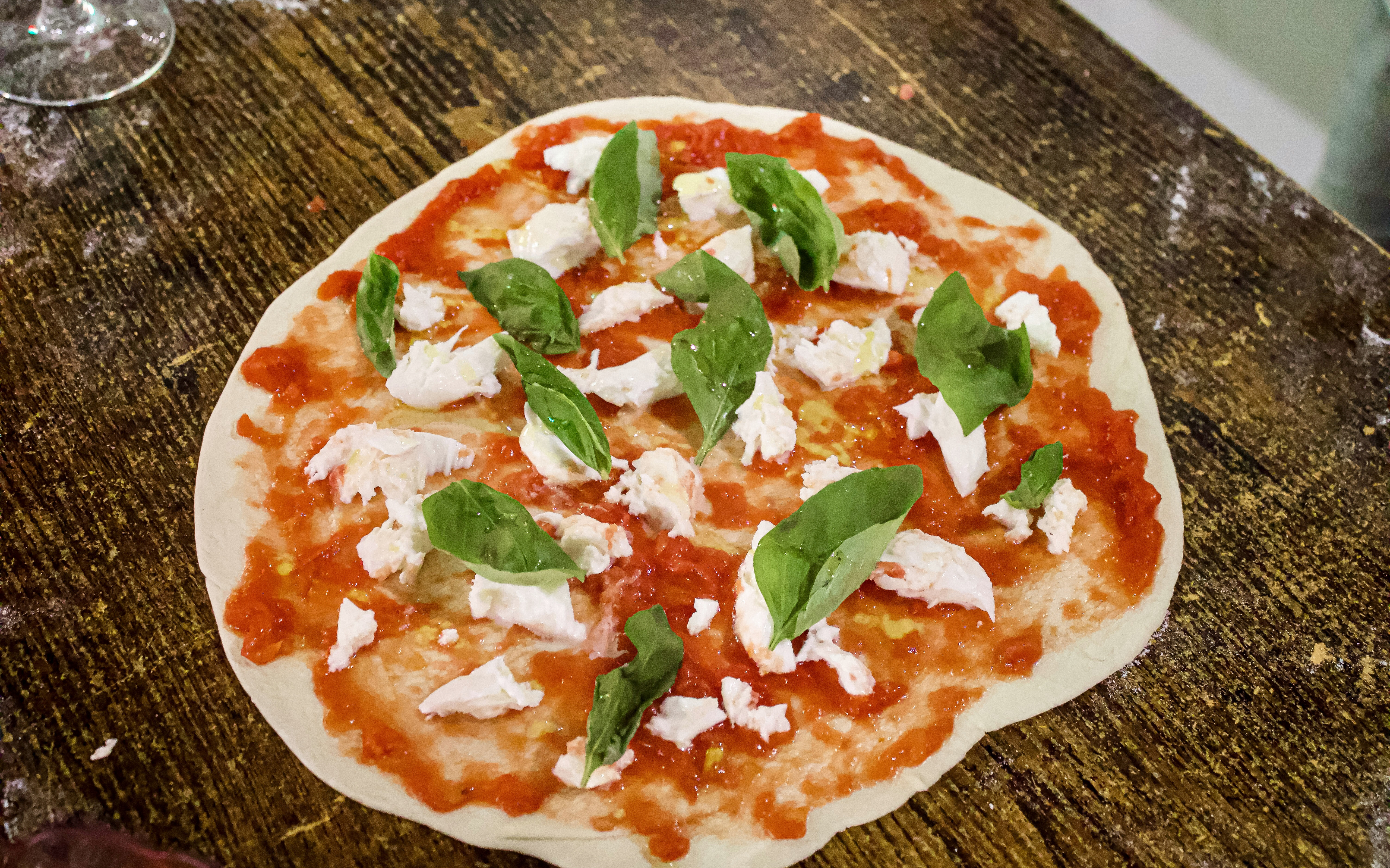 Pizza dough with tomato sauce, mozzarella, and basil leaves during Rome cooking class.