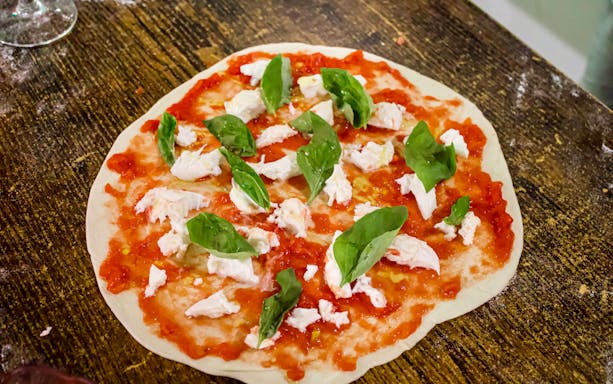 Pizza dough with tomato sauce, mozzarella, and basil leaves during Rome cooking class.