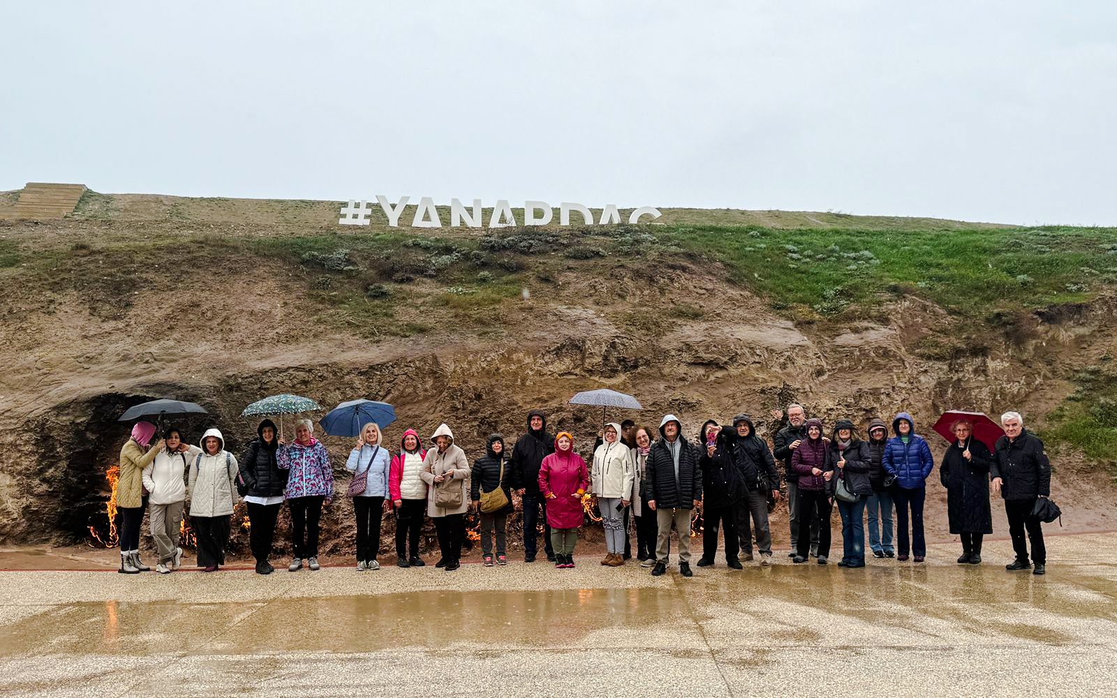 Group of tourists with umbrellas at Yanardag, Azerbaijan, near burning hillside.