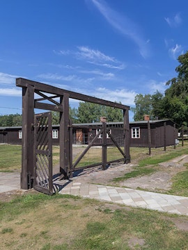 Entrance gate of Stutthof Concentration Camp with wooden barracks in the background.