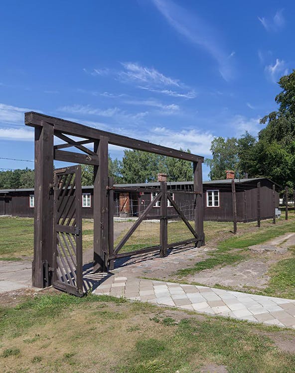 Entrance gate of Stutthof Concentration Camp with wooden barracks in the background.