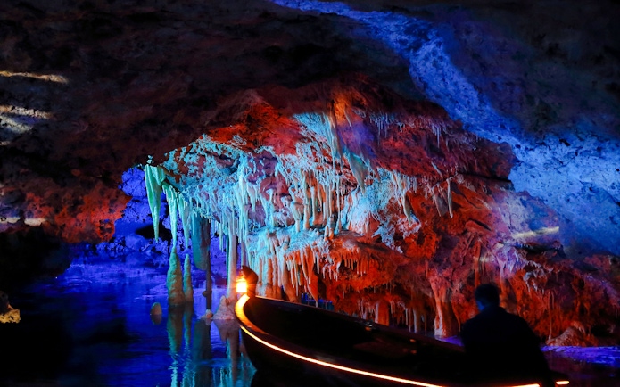 Boat tour inside illuminated Hams Caves, Mallorca, showcasing colorful stalactites.
