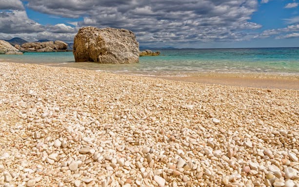 Pebble beach with clear turquoise water and rocky formations in Cala Mariolu, Sardinia.
