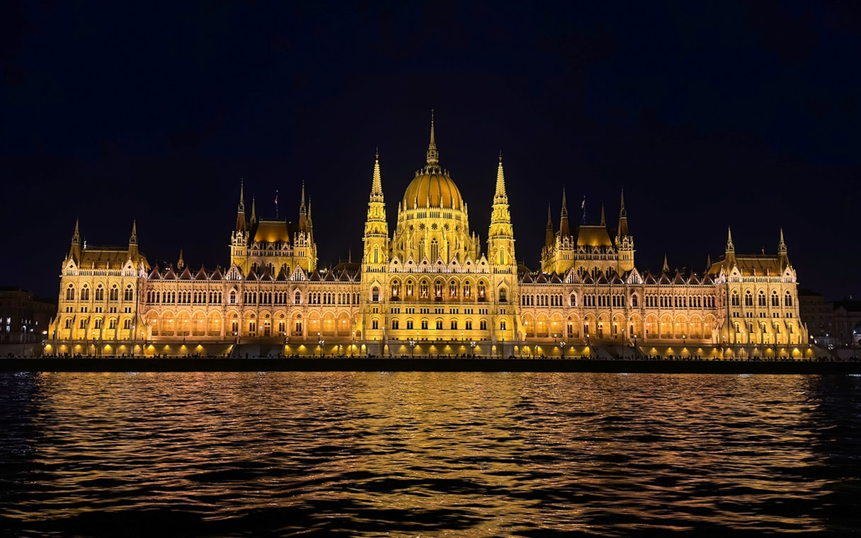 Hungarian Parliament Building illuminated at night, viewed from the Danube River.