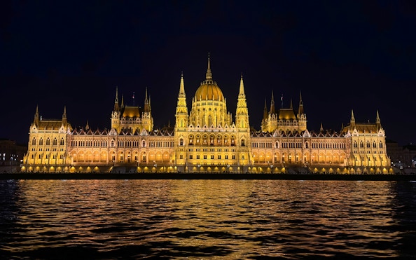 Hungarian Parliament Building illuminated at night, viewed from the Danube River.