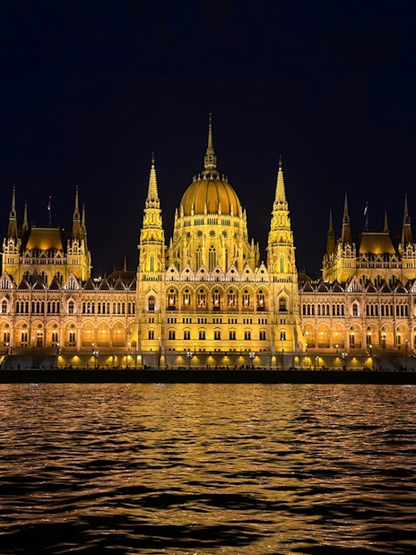 Hungarian Parliament Building illuminated at night, viewed from the Danube River.