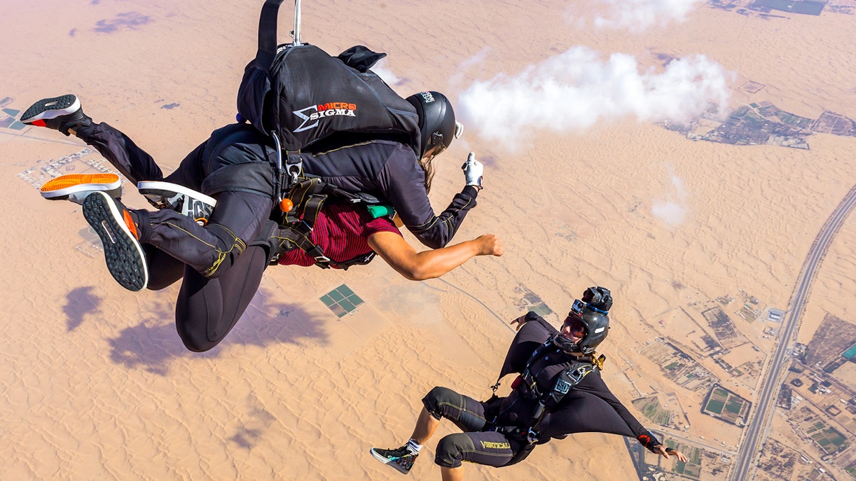 Tandem skydivers over Dubai desert landscape, capturing the thrill of freefall.